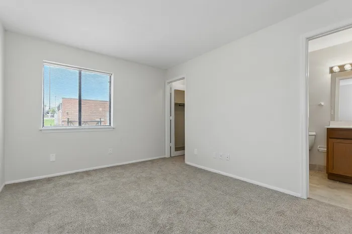 Bright and spacious bedroom with soft carpet flooring, featuring a large window and convenient en-suite bathroom access for modern living.