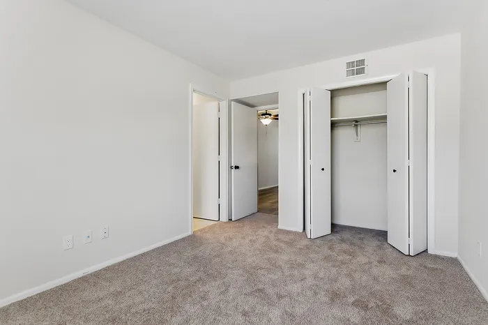 Bright spacious bedroom with plush carpet, large closet, and modern ceiling fan, offering ample storage and comfort.