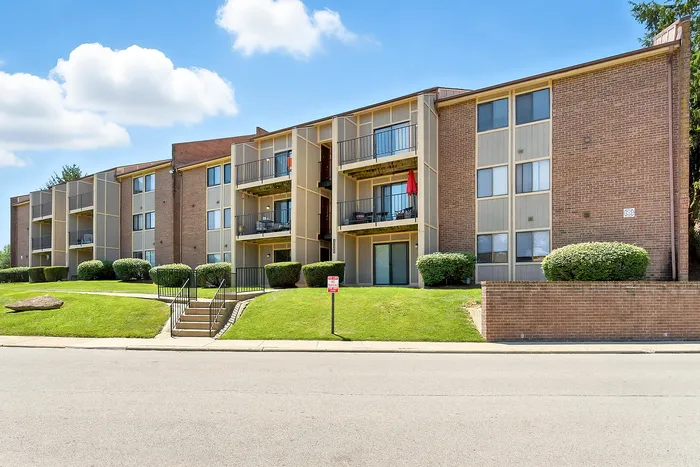 Modern apartment complex with stylish balconies, lush landscaping, and brick facade under a vibrant blue sky.
