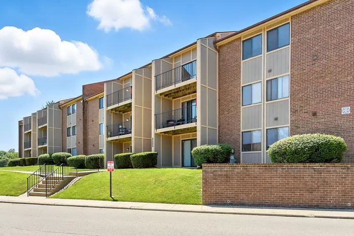 Charming apartment building with modern balconies, lush greenery, and sunny skies.