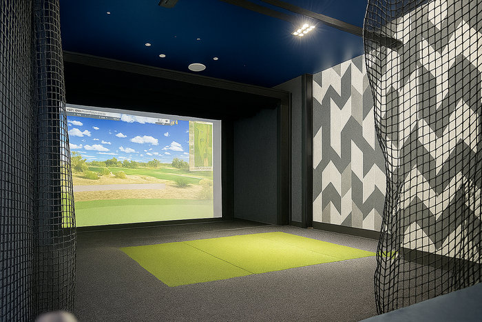 Modern indoor golf simulator room with vibrant green mat and high-definition virtual golf course display.