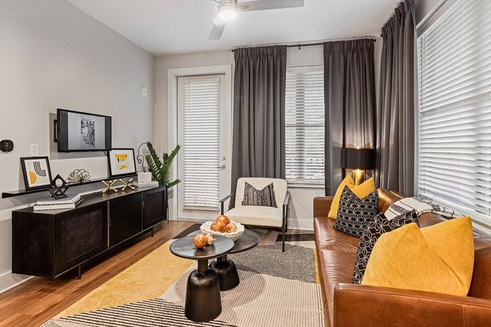 Chic living room with modern decor, featuring a sleek leather sofa with vibrant pillows, stylish artwork, and a cozy seating area with natural light.