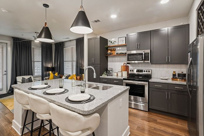 Modern open kitchen with sleek gray cabinetry, stainless steel appliances, and inviting granite breakfast bar overlooking a cozy living area with stylish decor.