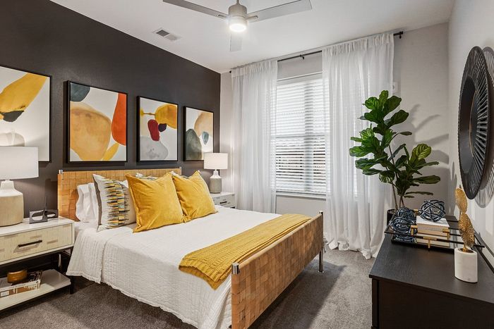 Modern and chic bedroom with stylish abstract artwork, cozy bed with yellow accents, and abundant natural light through large windows.