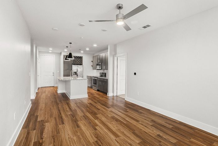 Chic modern kitchen with stainless steel appliances, elegant pendant lighting, and rich wooden flooring, flowing into a spacious open-concept area.