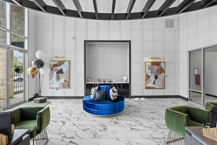 Elegant lobby featuring a modern blue velvet circular sofa, marble flooring, abstract artwork, and luxurious green velvet chairs under a stylish ceiling design.