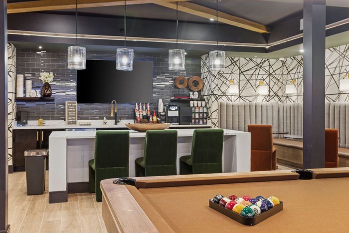 Luxurious apartment amenity space featuring a stylish lounge, modern kitchen with bar seating, and a pool table for entertainment.