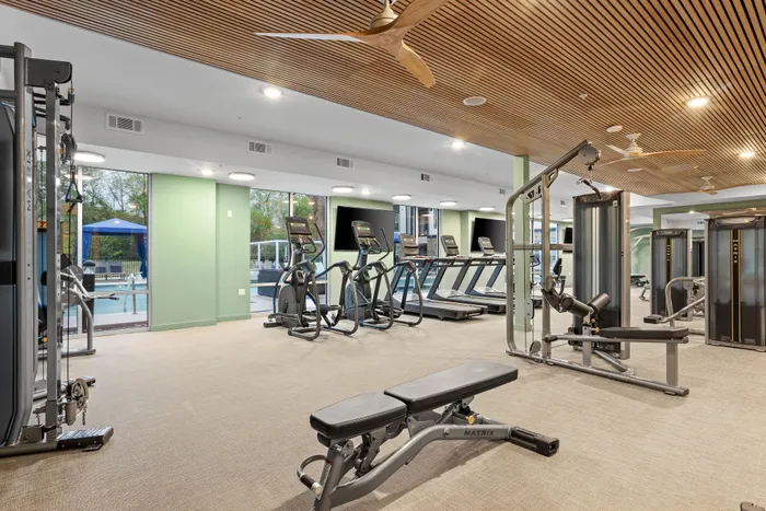 Modern fitness center with state-of-the-art gym equipment, treadmills, and exercise machines, overlooking a scenic outdoor pool area.