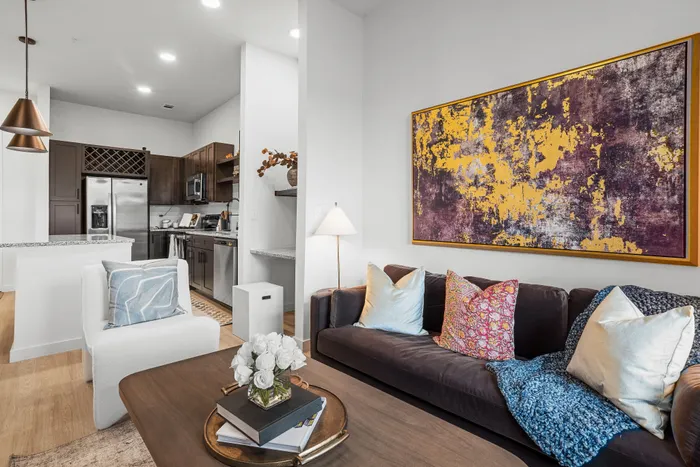 Modern living room featuring cozy seating, vibrant abstract art, and a sleek open kitchen with high-end appliances.