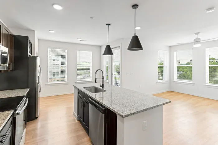 Bright and modern open-concept kitchen featuring sleek granite countertops, pendant lighting, and stainless steel appliances with ample natural light.