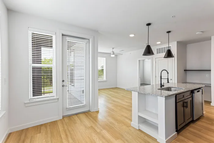 Modern open-concept living space with sleek kitchen island, elegant lighting, and natural light streaming through large windows.
