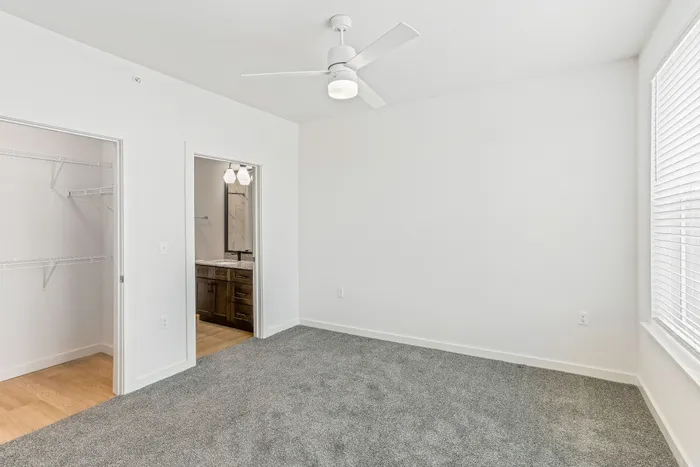 Bright bedroom with plush carpeting, modern ceiling fan, and attached bathroom featuring elegant vanity; includes a spacious walk-in closet for ample storage.