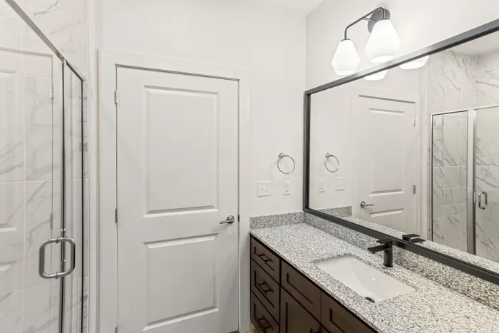 Contemporary bathroom with sleek granite countertop, large mirror, and elegant lighting above a stylish dark wood vanity.