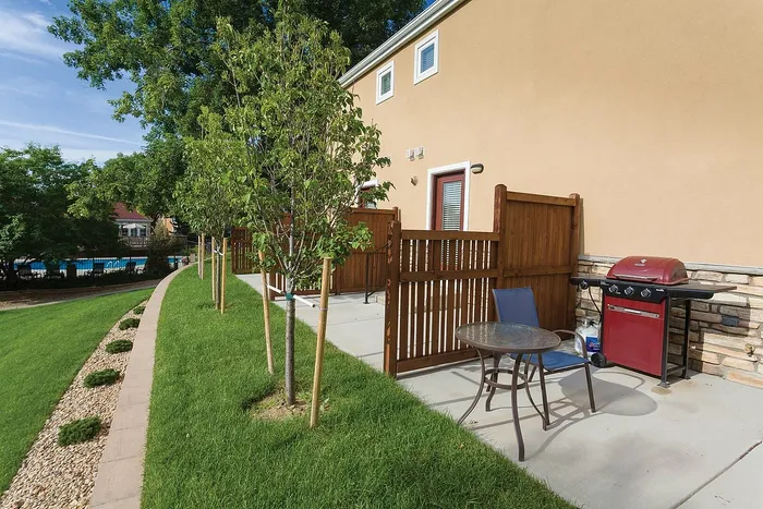 Charming patio with lush green lawn, wooden fencing, cozy seating, and a vibrant red barbecue grill inviting outdoor relaxation.