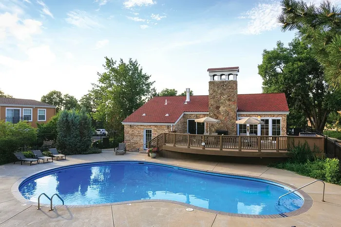 Charming stone house with red roof features a beautiful backyard pool, spacious wooden deck, and lush greenery.