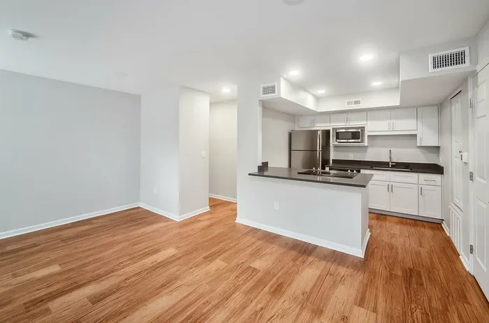 Modern apartment interior featuring sleek hardwood floors, open-concept kitchen with stainless steel appliances, and stylish white cabinetry.