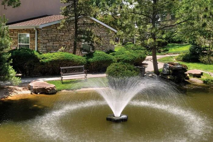 Charming garden scene featuring a stone building, a peaceful pond with a fountain, and lush greenery, perfect for serene living.