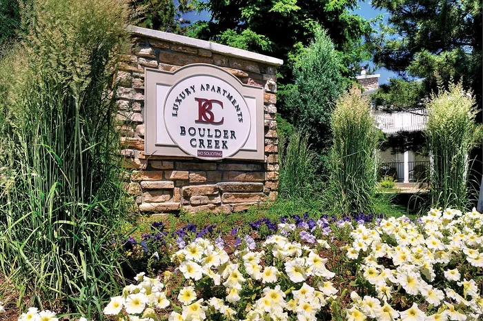 Elegant entrance sign for Boulder Creek Luxury Apartments surrounded by vibrant flowers and lush greenery, creating a welcoming atmosphere.