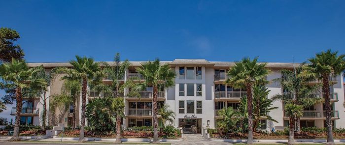 Elegant apartment building with lush palm trees and a serene facade under a vibrant blue sky.