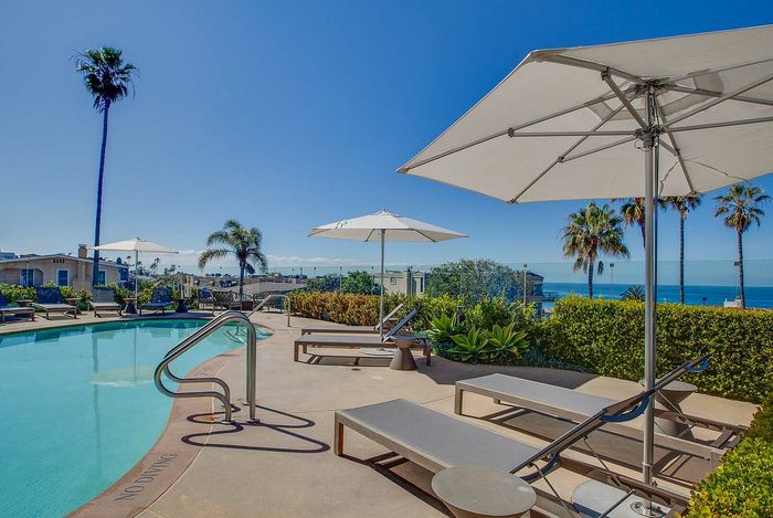 Luxurious outdoor pool area with sun loungers and umbrellas, offering a stunning ocean view and surrounded by vibrant greenery.