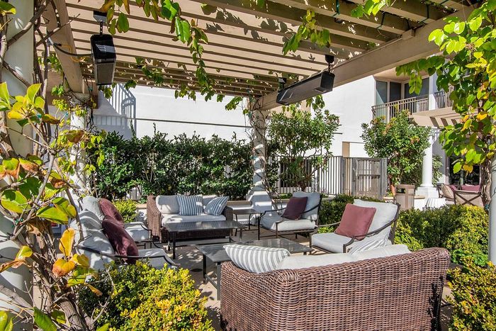Charming outdoor patio with cozy wicker furniture under a lush pergola, surrounded by vibrant greenery.