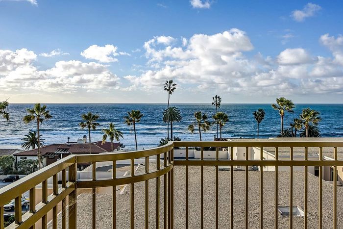 Breathtaking ocean view from a balcony, showcasing vibrant palm trees and a clear blue sky, perfect for a serene coastal living experience.