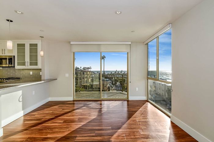 Modern apartment with sleek hardwood floors, open-concept kitchen featuring stylish lighting fixtures, and expansive windows offering stunning beachside views.