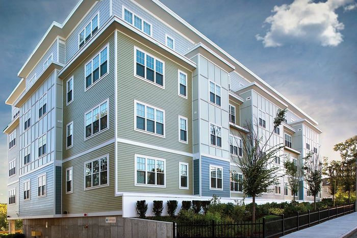 Modern apartment building with stylish siding, large windows, and manicured landscaping under a clear blue sky.