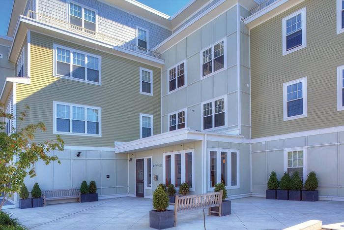 Inviting apartment exterior with charming architectural details, featuring well-maintained shrubbery and welcoming benches in a sunny courtyard setting.