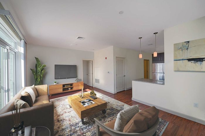 Bright and inviting living room with sleek modern decor, large windows, cozy seating, and an open-plan design leading to a stylish kitchen area.