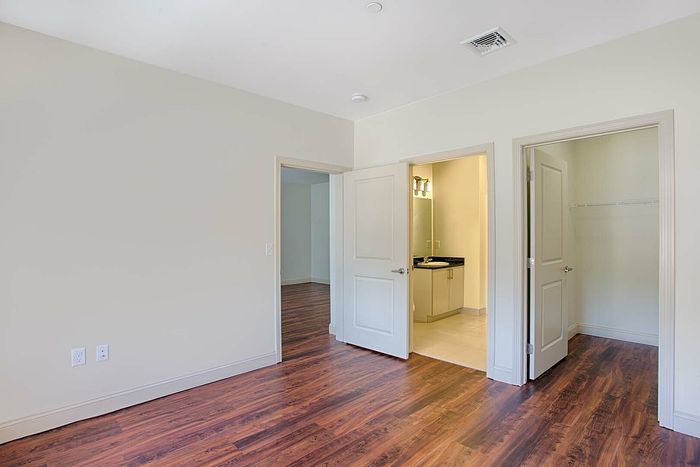 Bright and spacious bedroom with elegant wood flooring, connecting to a modern ensuite bathroom and a roomy walk-in closet.