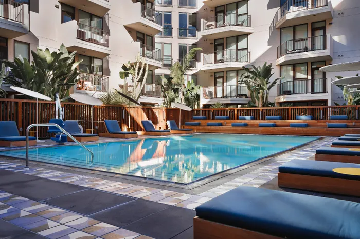 Luxurious apartment complex with a modern pool area, sun loungers, and lush greenery, offering a serene and stylish outdoor experience.