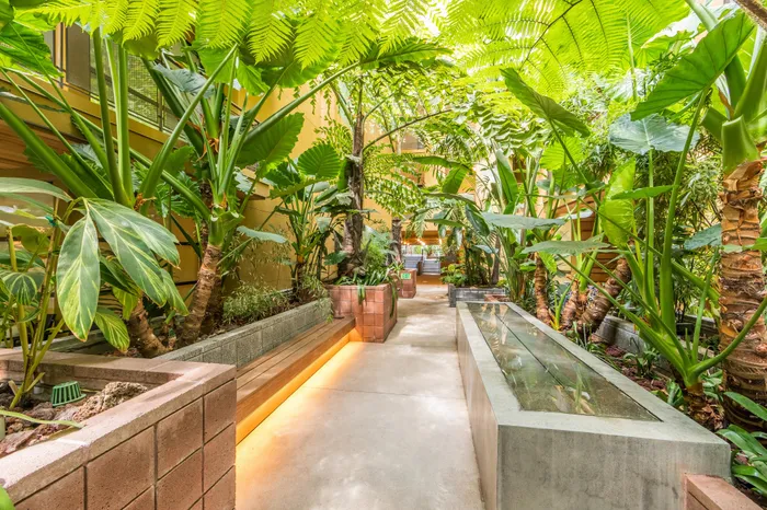 Lush green apartment atrium with tropical plants, illuminated walkways, and serene ambiance.