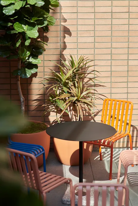 Charming outdoor patio with colorful chairs, lush potted plants, and a stylish black table against a modern brick wall.