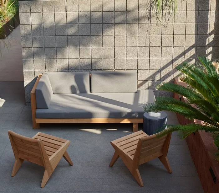 Chic outdoor patio with modern wooden furniture and lush greenery, perfect for relaxing and enjoying the sun.