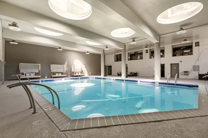 Luxurious indoor swimming pool with modern seating, natural light from circular skylights, and a serene atmosphere.
