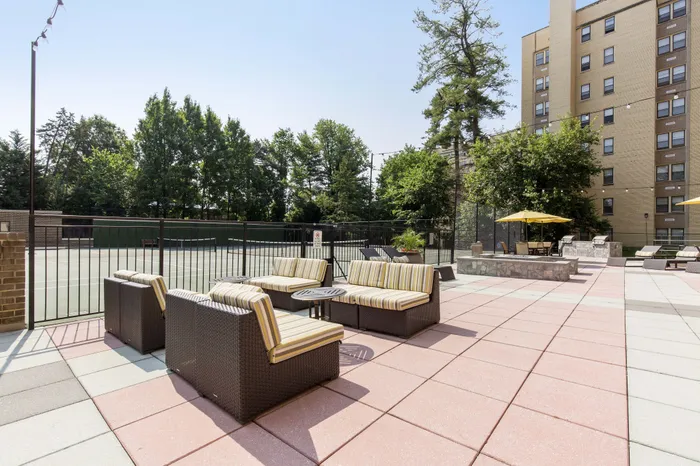 Chic outdoor patio with modern seating, surrounded by lush greenery and tennis court, perfect for relaxing and entertaining.