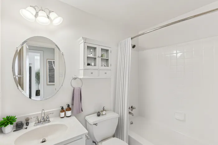 Elegant bathroom with modern fixtures, circular mirror, and sleek white tile design.
