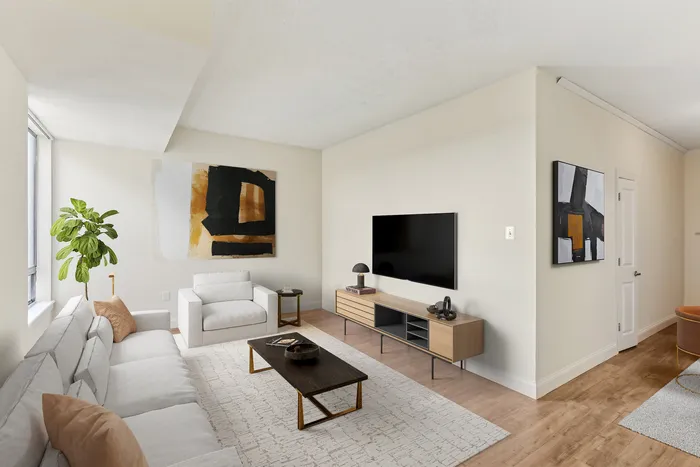 Elegant living room with modern decor, featuring a plush white sofa, abstract artwork, and a large flat-screen TV; perfect for stylish relaxation.