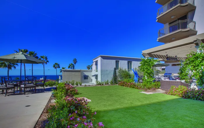 Exquisite ocean-view apartment with lush green lawns, vibrant flowers, and stylish outdoor seating under a pergola, perfect for relaxation and entertaining.