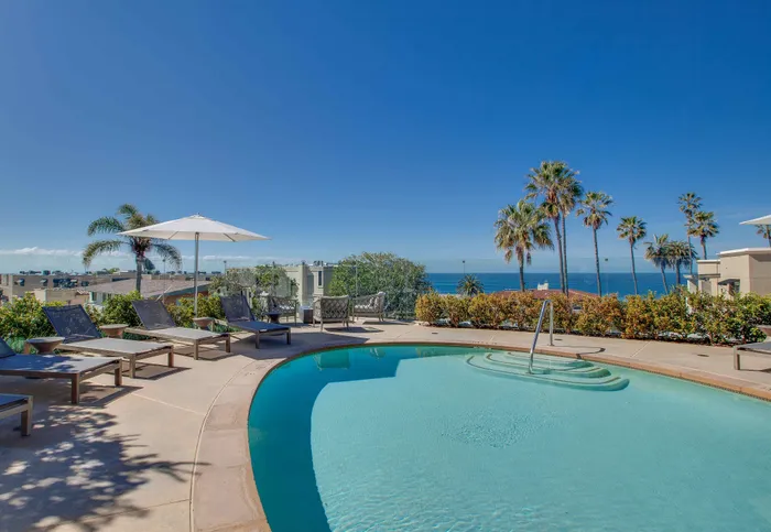 Luxurious poolside oasis with stunning ocean views, elegant lounge chairs, and tropical palm trees under a clear blue sky.