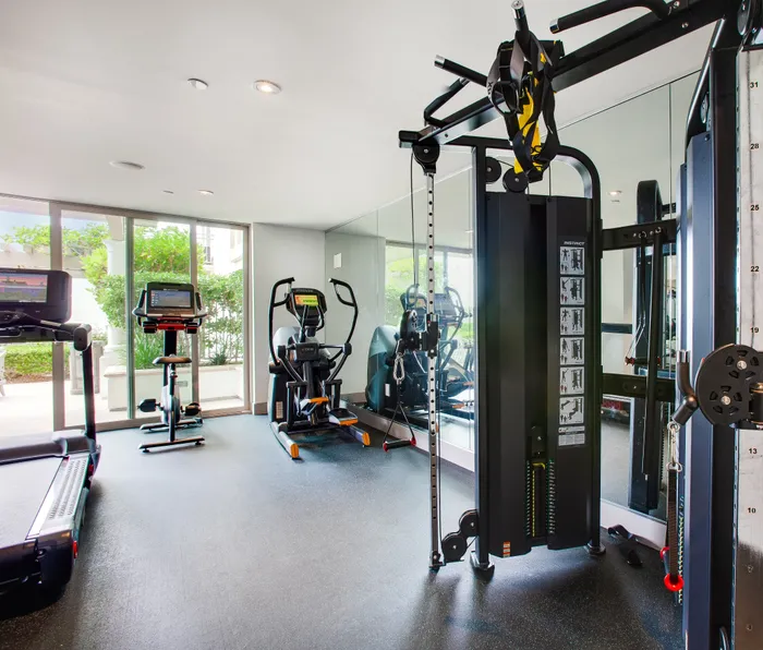 Bright and modern fitness center with state-of-the-art exercise equipment, featuring a treadmill, stationary bike, and weight machine, overlooking lush outdoor greenery.