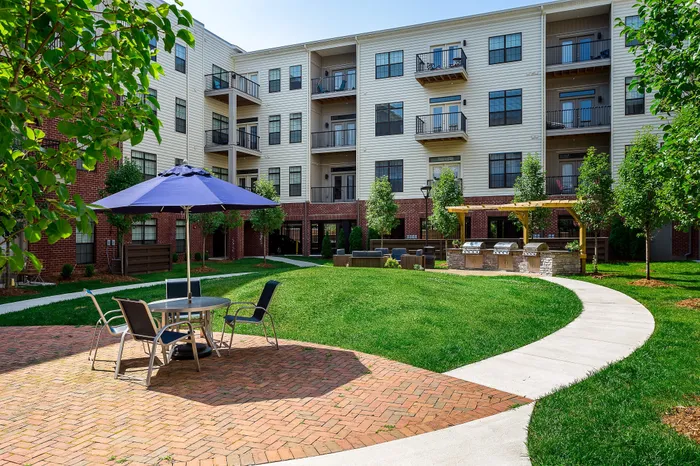 Charming apartment courtyard featuring lush green landscaping, cozy seating areas, and modern outdoor grills, perfect for relaxing and entertaining.