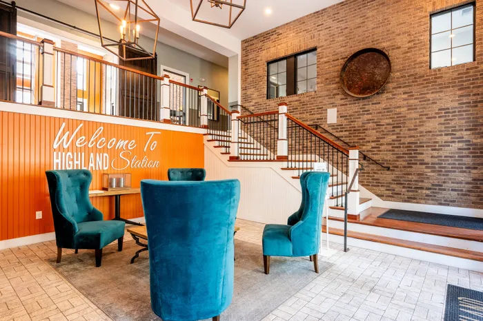 Welcoming lobby at Highland Station featuring elegant teal armchairs, warm wood accents, and a stylish stairway, setting a luxurious tone for the residence.