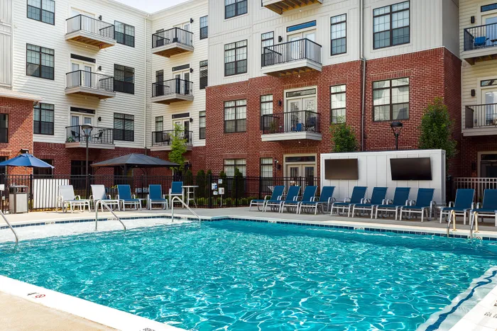 Modern apartment complex with a refreshing outdoor pool, surrounded by lounge chairs and stylish brick and siding architecture.