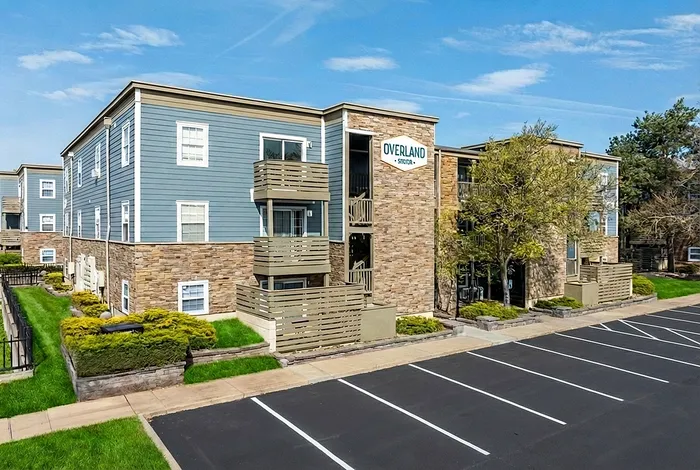Charming apartment complex with modern architecture, featuring elegant stone facades, balconies, and lush landscaping under a bright blue sky.