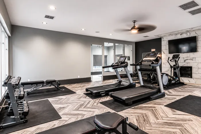 Modern fitness center with state-of-the-art treadmills, exercise bikes, and a set of free weights on sleek wood flooring, ideal for an active lifestyle.
