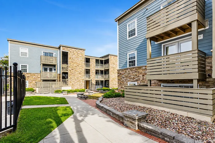 Beautiful modern apartment building with stone and wood facade, featuring multiple balconies and lush landscaped pathways.