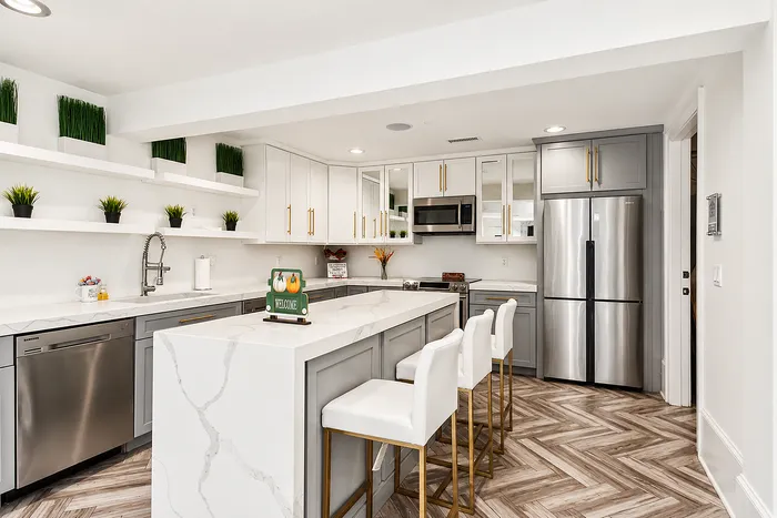 Modern kitchen with elegant white cabinetry, spacious marble countertop island, and stylish stainless steel appliances. Features chic open shelving and comfortable high-back bar stools.