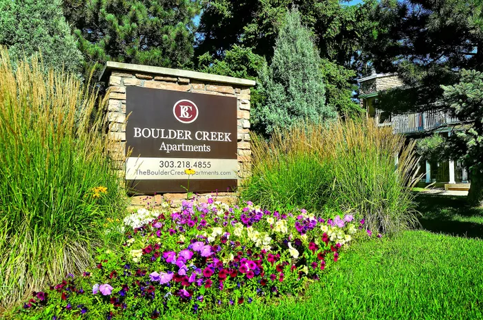 Welcoming sign for Boulder Creek Apartments, surrounded by lush greenery and vibrant flowers, offering a serene living environment.